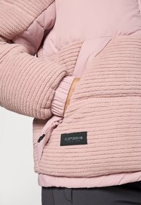Person wearing a pink textured fleece jacket with hand in side pocket and visible black label reading "ICEPEAK SINCE 1996."