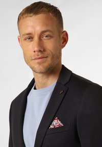 Schwarzer Blazer über einem hellblauen T-Shirt, mit einem gemusterten taschensquare in Rot, Weiß und Blau mit einem Union-Jack-Design.