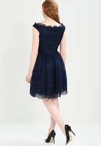 Navy blue dress with floral lace overlay, fitted bodice, scooped neckline, and full skirt. Notable scalloped hem and zipper closure at the back.