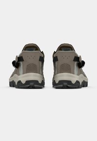 Καφέ αθλητικά παπούτσια από δίχτυ και σουέτ με μαύρες λεπτομέρειες, παχιά, υφή σόλα και ρυθμιζόμενους ιμάντες στο πίσω μέρος.