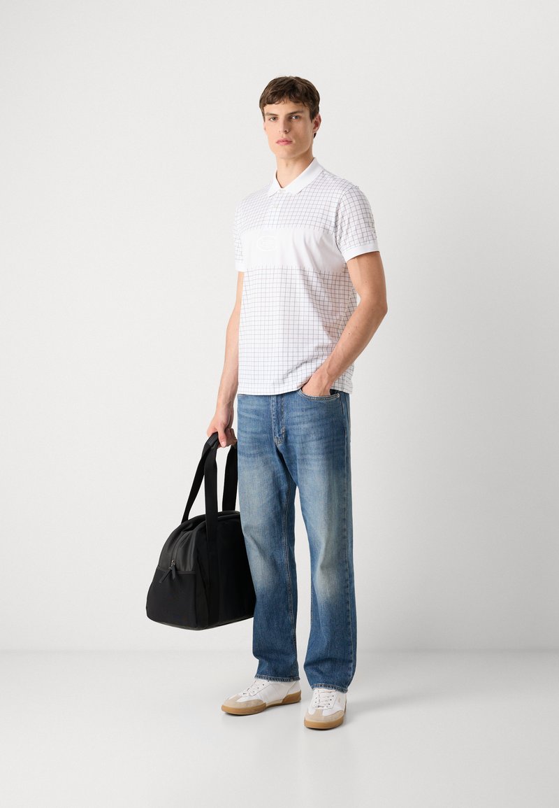 Camisa polo blanca con un patrón de cuadros, combinada con jeans de un tono azul claro y zapatillas blancas. Sosteniendo un bolso de deporte negro. Diseño simple, estilo casual.