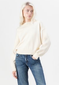 Crèmekleurige, cropped trui met een geribbelde halslijn en manchetten, gemaakt van zachte stof, gecombineerd met blauw jeans.