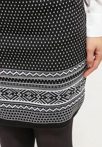 Svartvit stickad kjol med intrikata geometriska mönster, texturerat tyg och en tajt passform, som sträcker sig till mitten av låret.