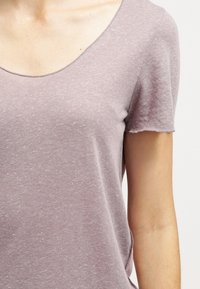 Ljuslila kortärmad topp med rundad halsringning, gjord av mjukt material, med en subtil melerad textur och avslappnad passform.