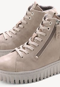 Beige korkeavartiset lenkkitossut, jotka on valmistettu nahasta ja joissa on sivuvetoketju, pyöreä kärki, teksturoitu pohja sekä teksturoituja yksityiskohtia päällisessä.