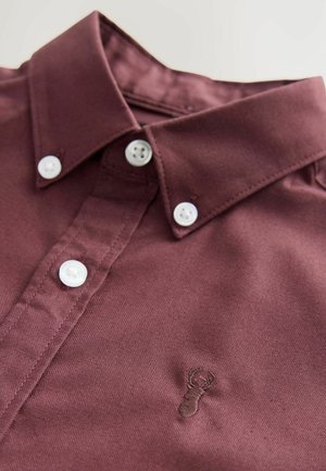 Chemise boutonnée bordeaux avec un col structuré, des boutons blancs et un petit logo de homard brodé sur le devant. Tissu doux et texturé.