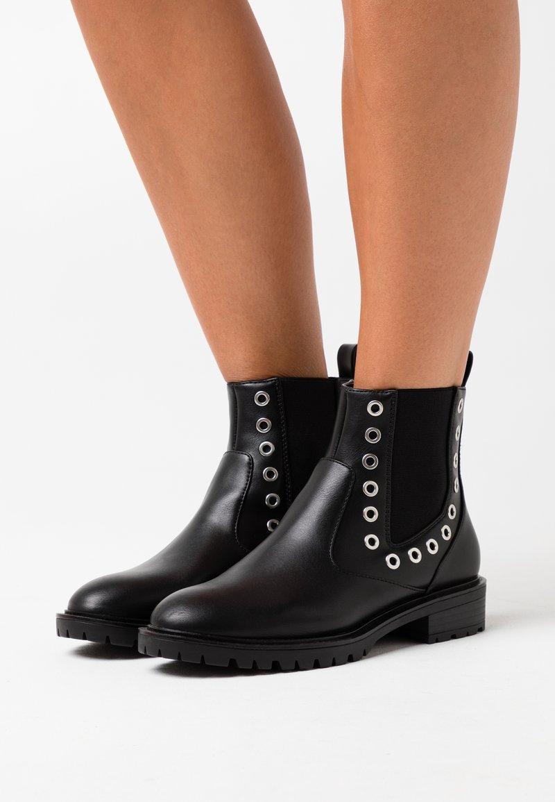 Černé kotníkové boty vyrobené z hladké kůže, s kovovými očky podél stran, elastickými panely a nízkými, texturovanými gumovými podrážkami.
