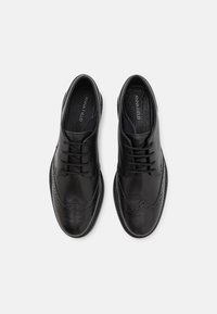 Scarpe da uomo in pelle nera con lacci, dettagli brogue, punta tonda e suola testurizzata, progettate per occasioni formali.
