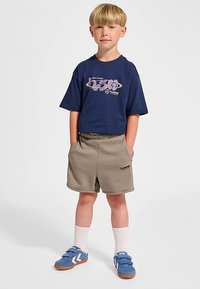 Marinblå t-shirt med tryck, beige shorts, blåa slip-on skor med vita strumpor. Avslappnad, bekväm passform och sköna material.