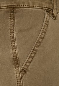 Khaki-kangas, jossa on sile�ä rakenne, etutasku ja huolellisesti ommellut saumat. Lähikuva, joka korostaa materiaalia.