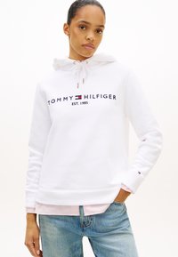 Biała bluza z kapturem z nadrukiem "TOMMY HILFIGER EST. 1985" w kolorze granatowym. Posiada troczki, ściągacze na rękawach oraz warstwowy, różowy pasek na dole.