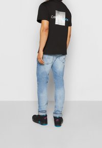 Černé bavlněné tričko s grafickým motivem na zádech, v kombinaci s světle modrými džínami a černými teniskami s modrými akcenty.