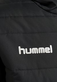 Giubbotto imbottito nero con texture trapuntata, caratterizzato da un grande logo bianco "hummel" sul fronte. Tessuto morbido e leggero.