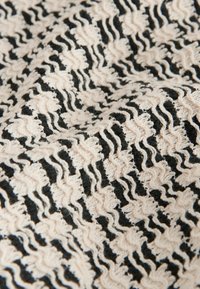 Gros plan sur un tissu tricoté noir et blanc texturé avec des motifs en zigzag ondulés en relief créant un effet tridimensionnel.