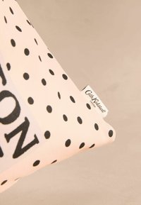 Bavlněný polštář s růžovým pozadím a černými puntíky, s bílou etiketou s nápisem "Cath Kidston" černým písmem.