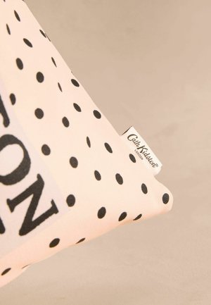 Kokvilnas spilventiņš ar rozā fona un melnām punktiņām, ar baltu etiķeti, uz kuras ir melnā krāsā uzrakstīts "Cath Kidston".