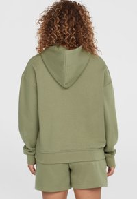 Olivegrüner Hoodie mit Kapuze und überschnittenen Schultern, aus weichem Stoff gefertigt. Mit gerippten Bündchen und Saum, kombiniert mit passenden Shorts.