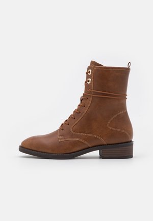 Bottines en cuir marron avec un bout rond, un laçage à l'avant et des œillets dorés. Elles présentent un petit talon empilé et des détails de couture subtils.