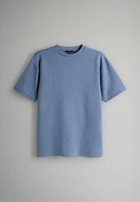 T-shirt à manches courtes bleu clair avec une texture côtelée et un col rond, présentant une coupe décontractée sans logos ni motifs visibles.
