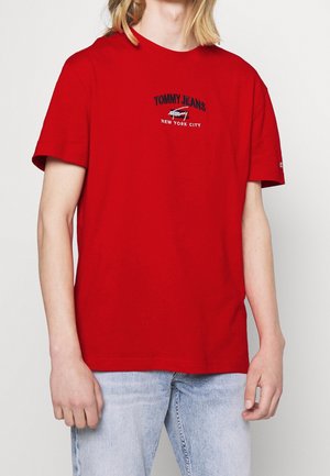 Rood katoenen T-shirt met korte mouwen, met de borduursels "TOMMY JEANS" en "NEW YORK CITY" in het zwart. Gecombineerd met lichtblauwe jeans.