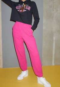 Black cropped hoodie with logo, paired with pink ribbed sweatpants and white sneakers. Smooth fabric and relaxed fit.