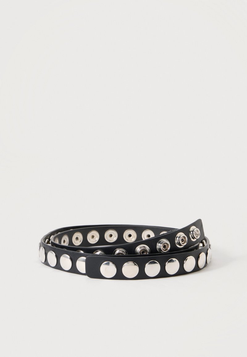 Ceinture noire avec deux rangées de grands clous ronds argentés, enroulée sur un fond blanc uni.