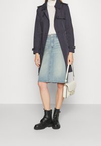 Marinblå trenchcoat, ljusgrå turtleneck, denim midi kjol, svarta snörstövlar och en vit axelremsväska. Slät material, klassisk design.