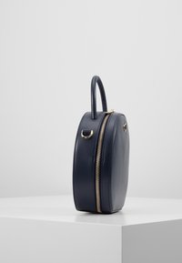 Borsa in pelle blu navy dalla forma arrotondata, con manico superiore e zipper dorato. Texture liscia con accenti di design circolare sui lati.