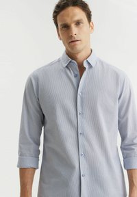 Jasnoniebieska koszula w paski wykonana z miękkiego materiału, z kołnierzykiem zapinanym na guziki, długimi rękawami podwiniętymi przy mankietach i jasnoniebieskimi guzikami.