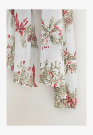 Biały materiał z kwiatowym wzorem ostrokrzewu, czerwonymi jagodami i czerwonymi wstążkami z zielonymi akcentami, delikatnie układający się w fałdy.