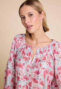 Blomstret bluse i lett stoff med et rosa og aqua blomsterprint, samlet halslinning og nøkkelhullsdetalj ved brystet. Lange ermer.