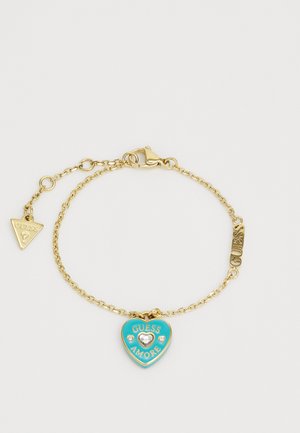 Gold chain bracelet featuring a heart charm with turquoise enamel, "GUESS AMORE" text, and a small crystal accent. Includes a triangle tag.