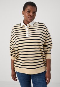 Gulrandig tröja med marinblå horisontella ränder, vit krage, knappslå och uppvikta ärmar. Tillverkad av mjukt, texturerat tyg.