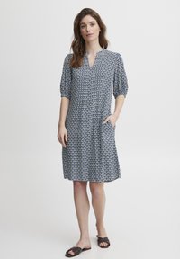 Modrá a bílá vzorovaná šaty s véčkovým výstřihem, krátkými nabíranými rukávy a kapsami. Vyrobeno z lehkého materiálu, do délky ke kolenům s uvolněným střihem.