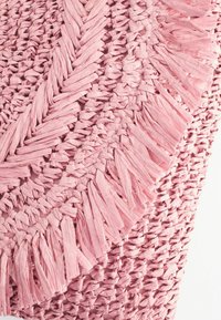 Sac en raphia tissé rose avec motif tressé circulaire et détails à franges sur fond blanc.