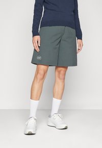 EA7 tamsūs pilki sportiniai šortai su šoninėmis kišenėmis, logotipo detale ir laisvu siluetu, derinami su baltais sportiniais batais ir kojinėmis.