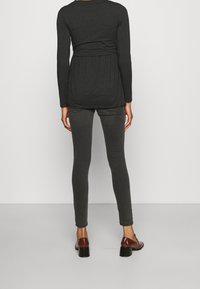 Mörkgrå långärmad topp med plisserad rygg, kombinerad med mörkgrå skinny jeans och bruna klackskor. Slät textur, figurnära design.