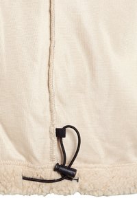 Beiges Kleidungsstück mit Fleece-Futter, strukturiertem Außenstoff, kontrastierendem weichem Pelzsaum und schwarzem Kordelzug am unteren Rand.