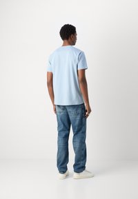 Lichtblauwe katoenen t-shirt met korte mouwen, gecombineerd met blauwe denim jeans. Model draagt witte sneakers. Eenvoudig, casual ontwerp.