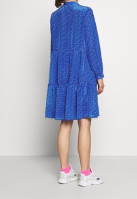 Blå blommig klänning med långa ärmar, lagerdesign och mjukt tyg. Bärs med vita sneakers och ljusrosa strumpor.