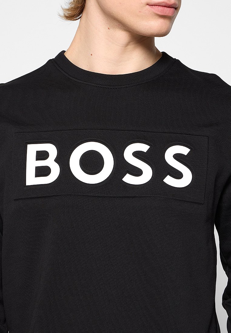 Maglietta nera a maniche lunghe realizzata in tessuto testurizzato, con un grande logo bianco "BOSS" su un patch rettangolare sul davanti.