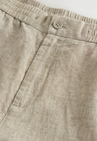 Pantalones cortos de lino beige con cintura elástica y cierre de botón, con una textura suave y fibras naturales sutiles visibles.