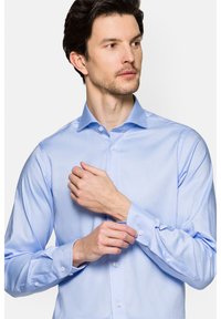 Jasnoniebieska koszula z długim rękawem, uszyta z gładkiego materiału, z kołnierzykiem typu spread i mankietami na guziki, o dopasowanym kroju i minimalną teksturą.