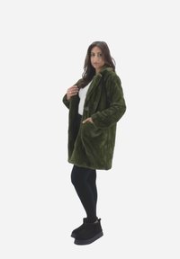 Cappotto in pelliccia sintetica verde con una vestibilità ampia, colletto largo e maniche lunghe. Abbinato a leggings neri e stivali alla caviglia.