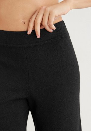 Pantalon en maille noire avec une texture lisse et une taille élastique, présentant un design ajusté. Le tissu est doux et légèrement extensible.