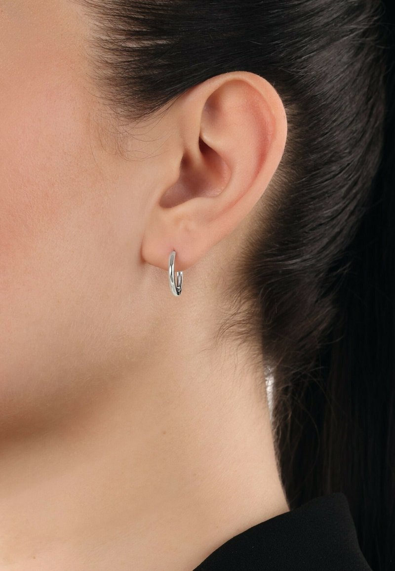 Orecchino a cerchio in argento con un design elegante e curvo. Superficie riflettente con una finitura lucida, montato nel lobo dell'orecchio.