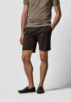 Braune Baumwollshorts mit klassischer Passform, Seitentaschen und vorderem Reißverschluss, kombiniert mit dunkelbraunen Slippern.