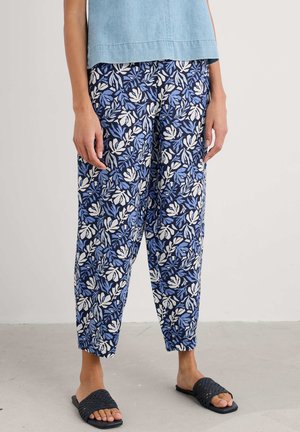 Lichte blauwe en witte bloemenpatroonbroek met een taps toelopende pasvorm, voorzien van een elastische tailleband, gecombineerd met zwarte slidesandalen.