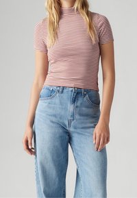 Punainen ja valkoinen raidallinen korkeakauluksinen paita, yhdistettynä vaaleansinihin leveälahkeisiin farkkuihin. Lyhyet hihat ja sileä kangas istuvalla leikkauksella.