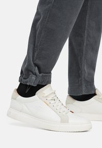 Witte leren sneakers met lichtbruine accenten en een gestructureerde suede hiel. Gepaard met grijze corduroy broeken, die iets verzameld zijn bij de boorden.